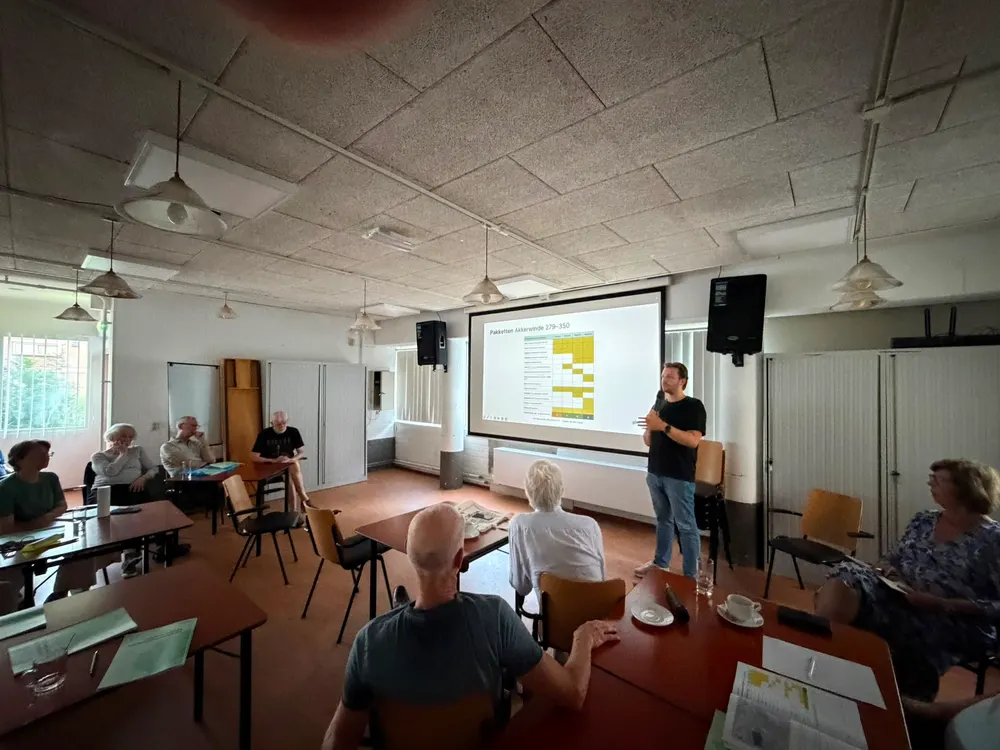 Een bijeenkomst in een zaal, met de presentatie op het scherm vooraan