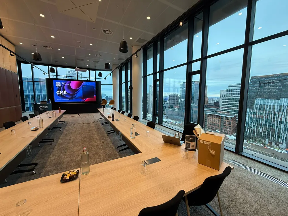 Een lange vergadertafel met scherm, en uitzicht over de stad