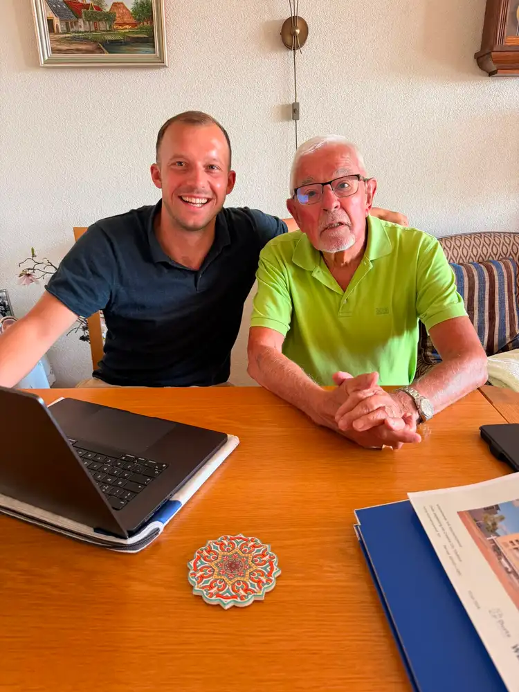 Twee mensen in gesprek aan tafel, met een laptop tussen hen in
