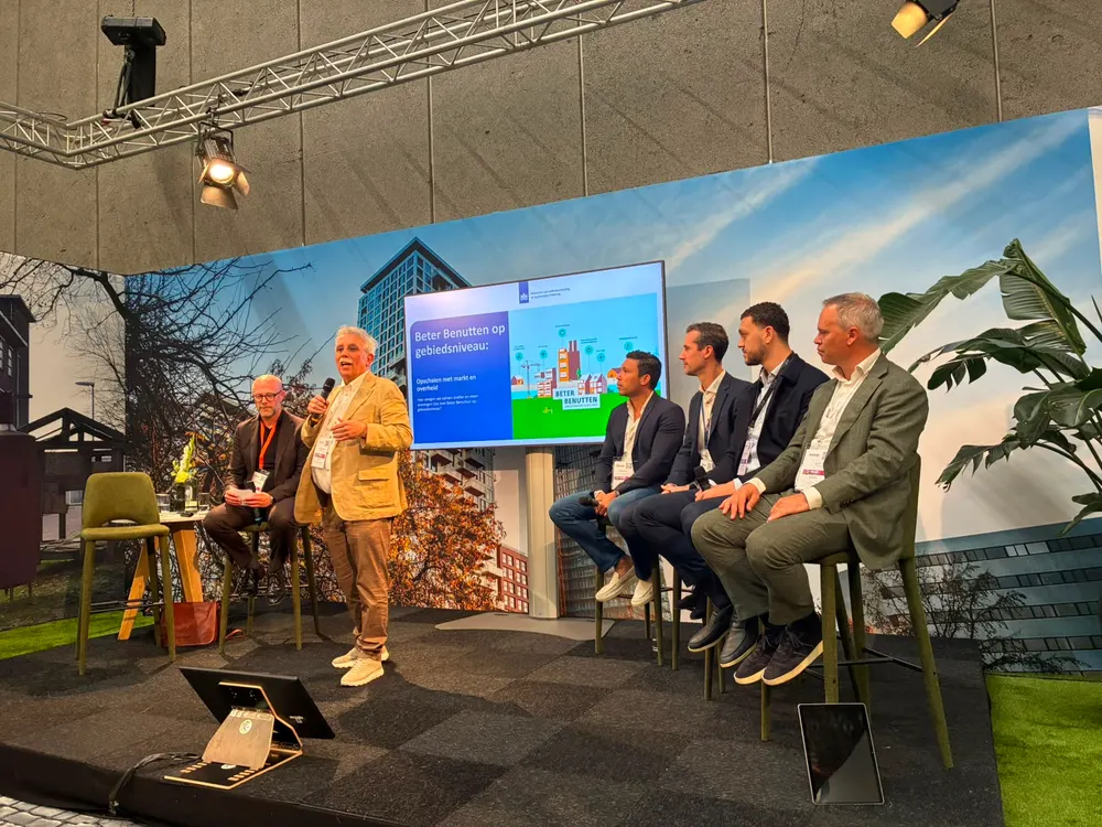 Een paneelgesprek op een podium, met een landschapsfoto als achtergrond