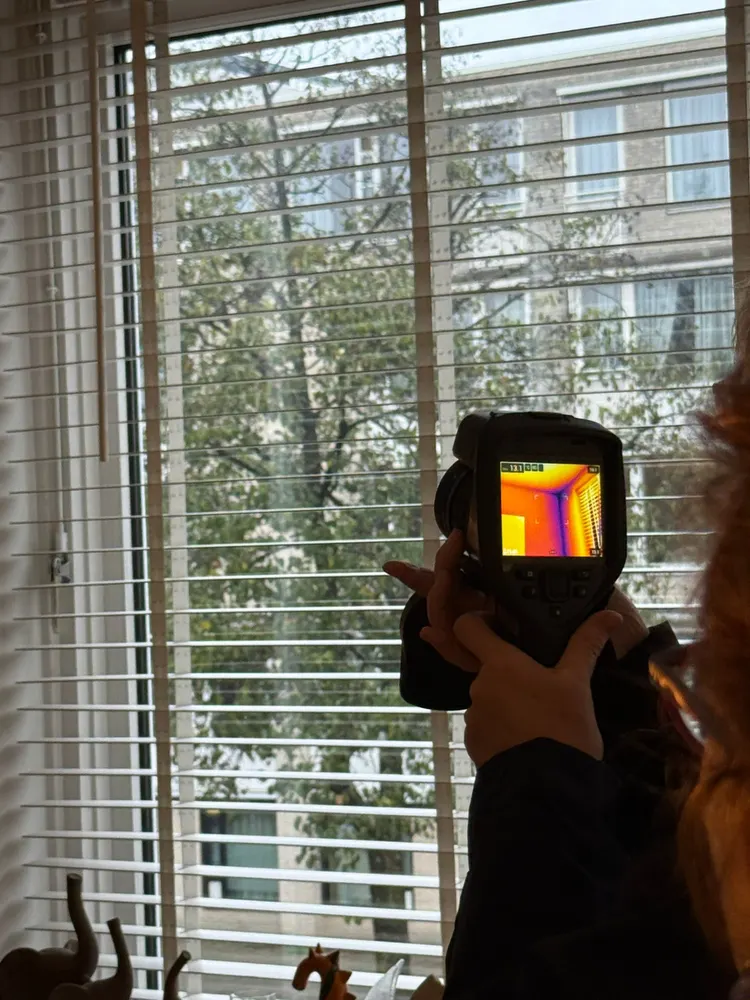 Een warmtebeeldcamera gericht op een raam, met de warmte in kleur op het schermpje